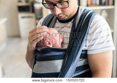 Close up of young father with his newborn baby son in sling at home