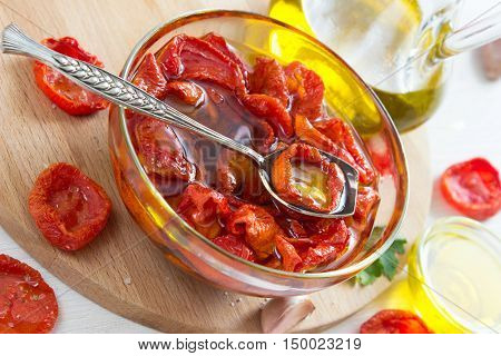 homemade dried tomatoes in glass bowl with ingredients on wooden desk