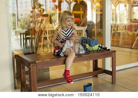 Cuite smiling little girl is putting of rain boots in the playschool