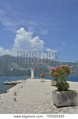 The artificially created island Our Lady of the Rock island in Kotor Bay Montenegro. A small oleander plant can be seen in the foreground and a small lighthouse in the background