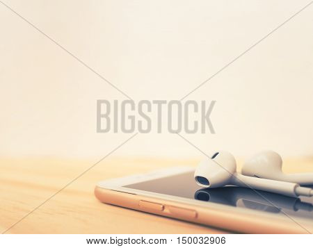 Close-up image of earbuds on top of smartphone and reflection on screen on wooden table with copy space. Cross process filter