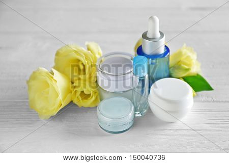 Cosmetic bottles and eustoma flowers on light wooden background
