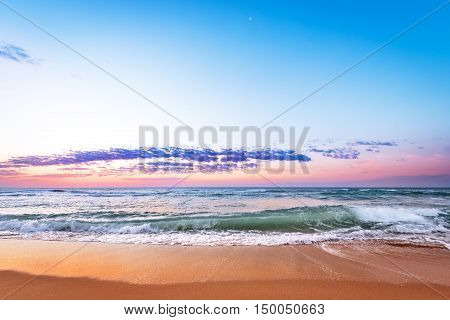 Sunrise light shining on ocean waves. Golden sands and blue sky