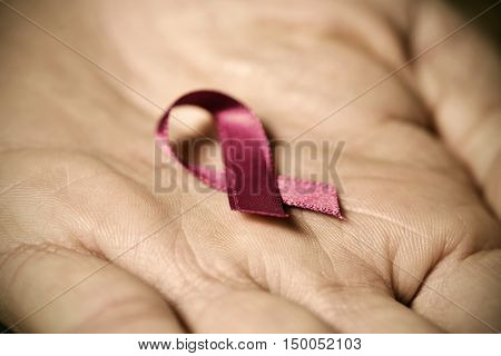 closeup of a pink ribbon for the breast cancer awareness in the palm of a man, with a dramatic effect