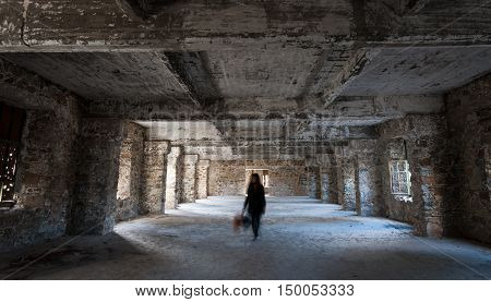 Unrecognized person walks like a ghost on an empty creepy abandoned hotel room with dramatic sun rays entering through the windows.