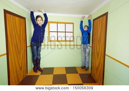 Boy and girl pose in room with optical illusion.