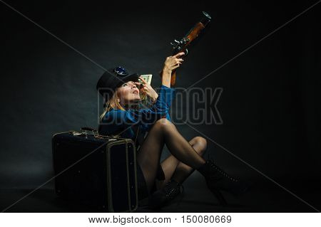 Fashionable subculture weapon concept. Steampunk girl with cash. Young gorgeous lady in victorian fashion lying on floor with banknotes briefcase and blunderbuss.