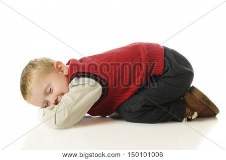 An adorable preschooler in slacks and a sweater vest, bottoms up feigning sleep.  On a white background.