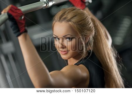 Fitness portrait of a young woman, abs close up. Girl doing back pullups at the gym, and looking at camera