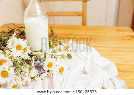 Simply stylish wooden kitchen with bottle of milk and glass on table, summer flowers camomile, healthy foog moring concept noone