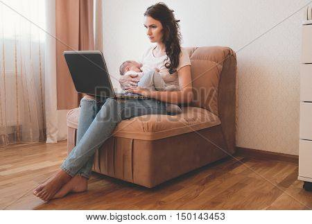 Beautiful young mother working with laptop computer and breastfeeding her newborn baby at home. Mom - business woman.