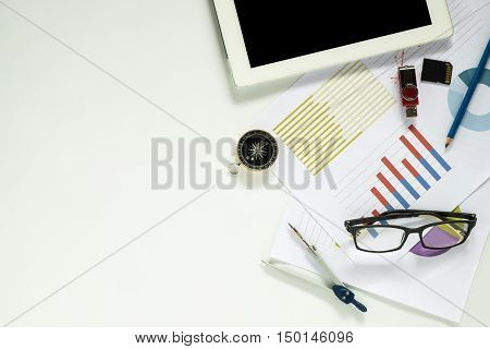White office desk table with blank screen tablet pencil flash drive sd card compass glasses and graph or analysis chart. Top view with copy space.Office desk table concept.