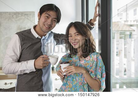 couples of asian young man and woman with coffee cup in hand standing relaxing in home living room