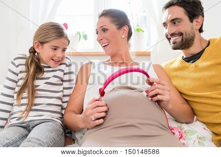 Father, daughter and pregnant mum using headphone for early musical intervention on mothers belly