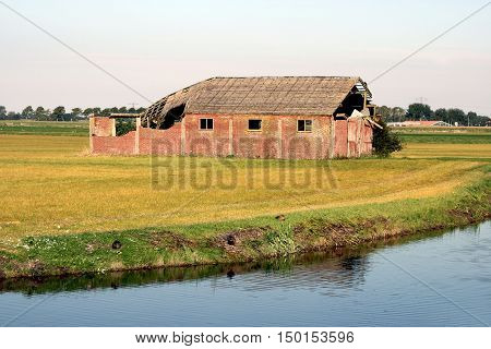 An old barn partially decayed. On a field near water.
