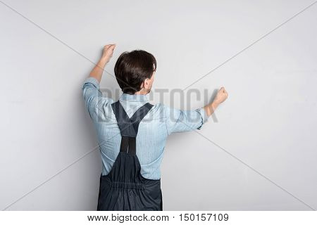 do it obligstory. Handsome goodloking man pretending like hanging picture and holding his hands up while standing against grey background.