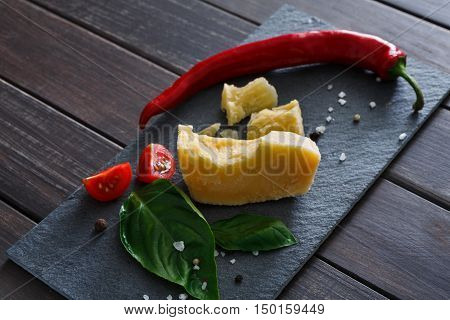 Cheese delikatessen closeup on rustic wood. Black stone desk with parmesan cuts decorated with chili, tomato and basil