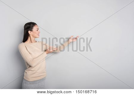 Just put your glance. Cheerful beautiful woman smiling and showing aside while standing isolated on grey background
