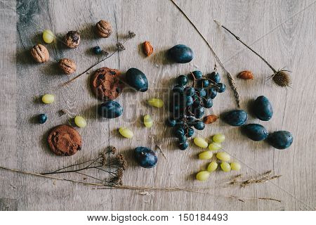lying on wooden background grapes plums dry grassthistlewalnuts biscuit.layflat