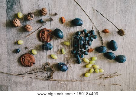 lying on wooden background grapes plums dry grassthistlewalnuts biscuit.layflat