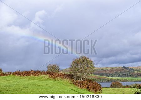 Beautiful colorful rainbow after the rain on stunning remote rural landscape on Isle of Skye Scotland. Loch and heather covered hills in the background.
