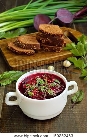 Red borscht soup with dill in white bowl on wooden table