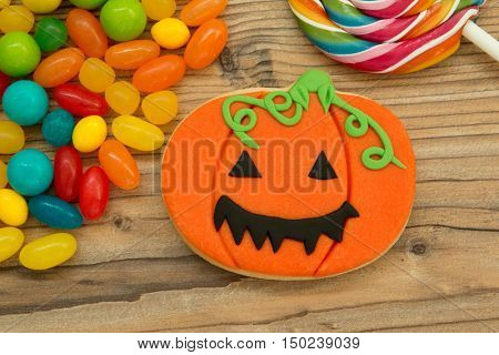 Smiling pumpkin cookie with many colorful candies on a wooden backgrund