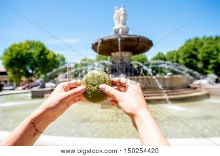 Female hands holding macaron cookie near the famous fontain de la Rotonde in Aix-en-Provence in France