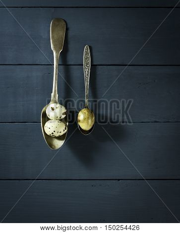 Quail eggs in old spoons. On a blue wooden background