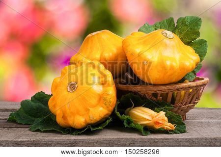 yellow pattypan squash with leaf in a wicker basket on a wooden table with a blurred background.