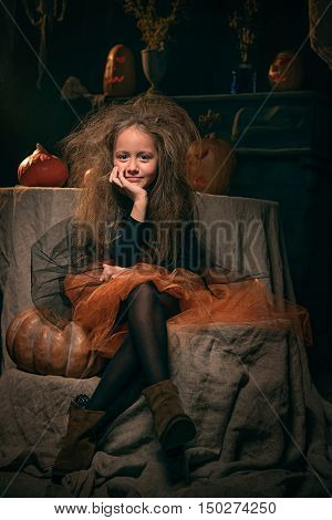 small girl in witch costume sit in helloween decoratios