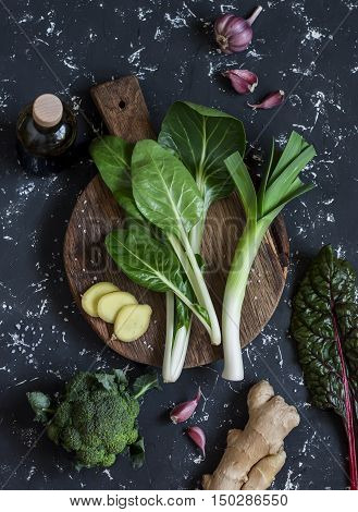Fresh ingredients - chard leeks ginger broccoli garlic soy sauce. On a dark background top view
