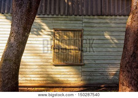 A closed window on an old storage wall. The autumn sun cast strong shadows on the wooden wall.