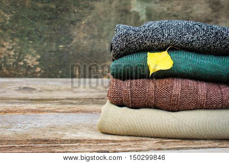 Pile of colorful warm clothes and yellow leaf on wooden background. Toned image.