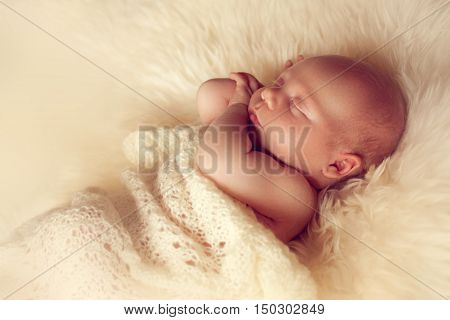 Sleeping newborn baby lying on white fur carpet covered with cream knitted blanket. The little boy fell asleep on the floor