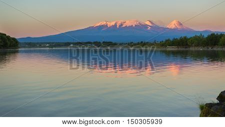 Sunset lighting Kluchevskaya group of volcanoes with reflection in the river Kamchatka.