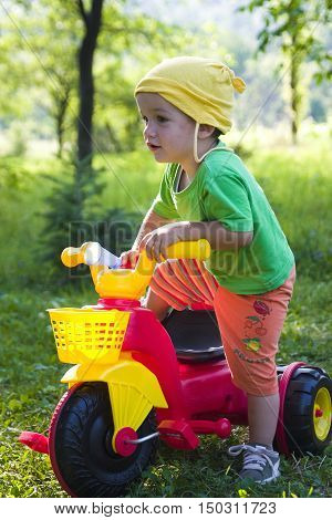 Child outside in garden with colorful toy tricycle