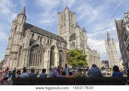 Ghent, Belgium, 27 august 2016: people sit on bench in shadow near st niklaaskerk
