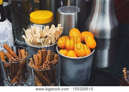 Making mulled wine for sale at country fair. Glintwine accesories, stirring wooden sticks, spices and citrus, cinnamon sticks and kumquat in metal bowls closeup.