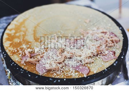 Making ham and cheese crepe at pan. Salty crepe or pancake with fillings made by street vendor's hands at outdoors creperie. French cuisine, cooking for commercial kitchen.