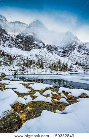 Winter day in Polish Tatra mountains, frozen Morskie Oko lake and summits in the clouds.