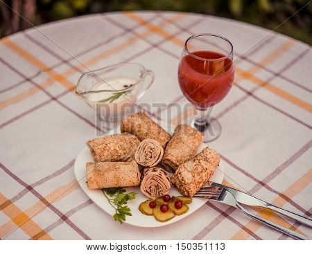 Tasty pancakes with meat on white plate closeup. Crepes stuffed with finely cut meat. glass of tomato juice and white sauce.