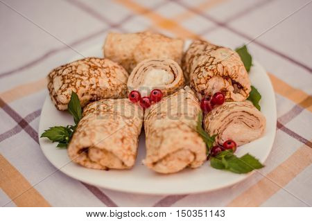 Tasty pancakes with home made cheese on white plate closeup. Crepes stuffed with cheese on checked table cloth.