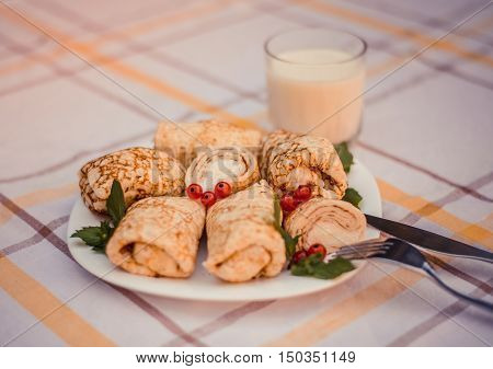 Tasty pancakes with home made cheese on white plate closeup. Crepes stuffed with cheese, and glass of milk on checked table cloth.