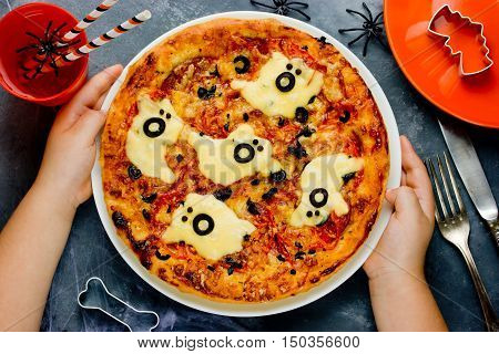 Child cooking pizza on Halloween. Funny ghost pizza with sausage cheese and olives top view