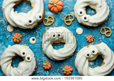 Halloween treats little monster dessert with donut dipped in white chocolate topped with chocolate eyes on a blue table with sweets and cookies Happy Halloween Background