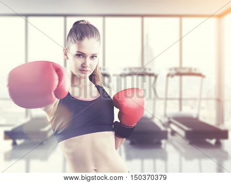 Confident woman boxer making a punch in gym with treadmills. Concept of competitive sports. Toned image
