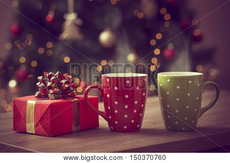 Nicely wrapped gift box and two cups of hot coffee set on the coffee table with the decorated Christmas tree in the background