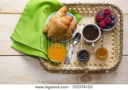 Black coffee orange juice berries and croissants with different jam for breakfast served in straw tray on wooden background. Top view.