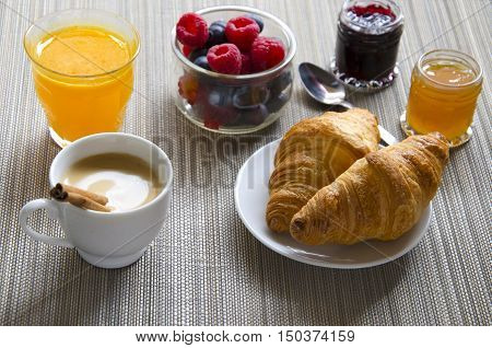 Black coffee orange juice berries and croissants with different jam on wooden grey background.